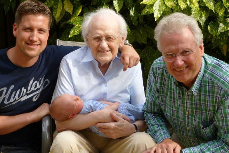 3 adult men smiling with the eldest holding an infant